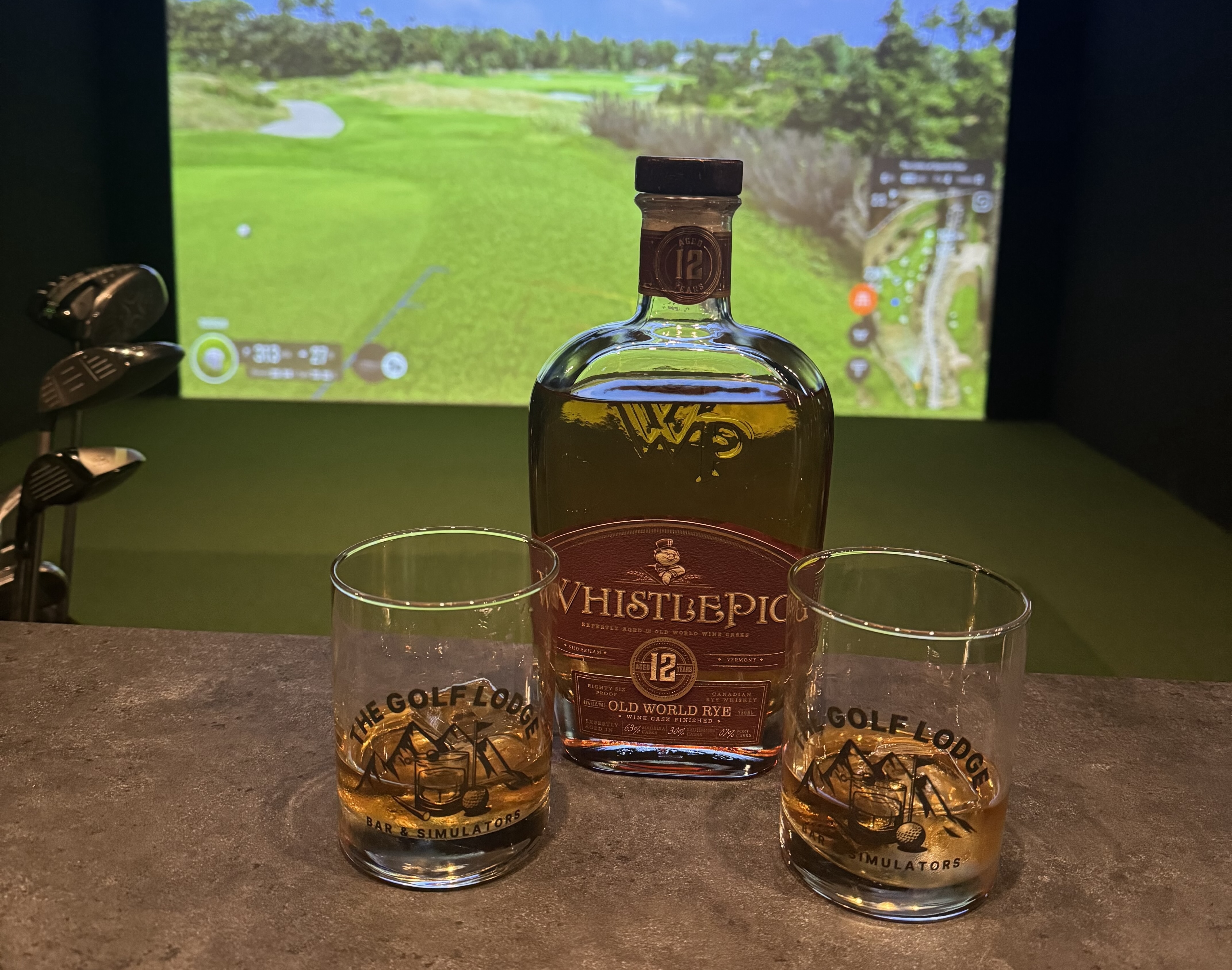 WhistlePig bourbon and Golf Lodge branded glasses in front of the Trackman simulator
